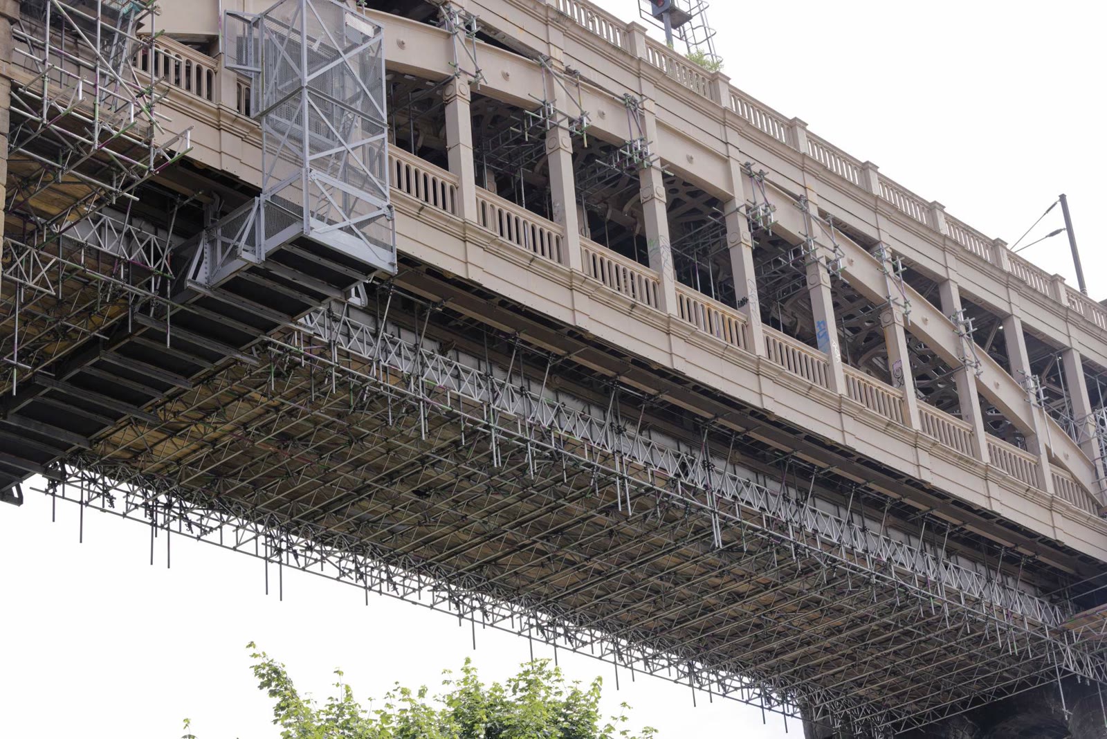 Wide riverside view of a historic double-deck bridge with scaffolding suspended beneath the deck