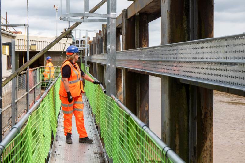 Worker in hi-vis on an elevated walkway beside steel bridge structure