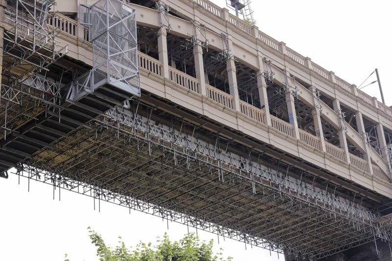 Wide riverside view of a historic double-deck bridge with scaffolding beneath the deck
