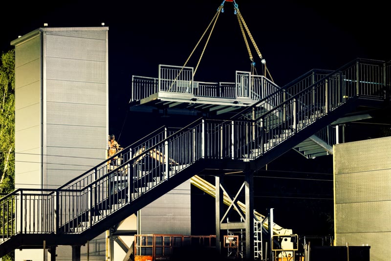 Night-time crane lift of a prefabricated lift shaft structure at a rail station site